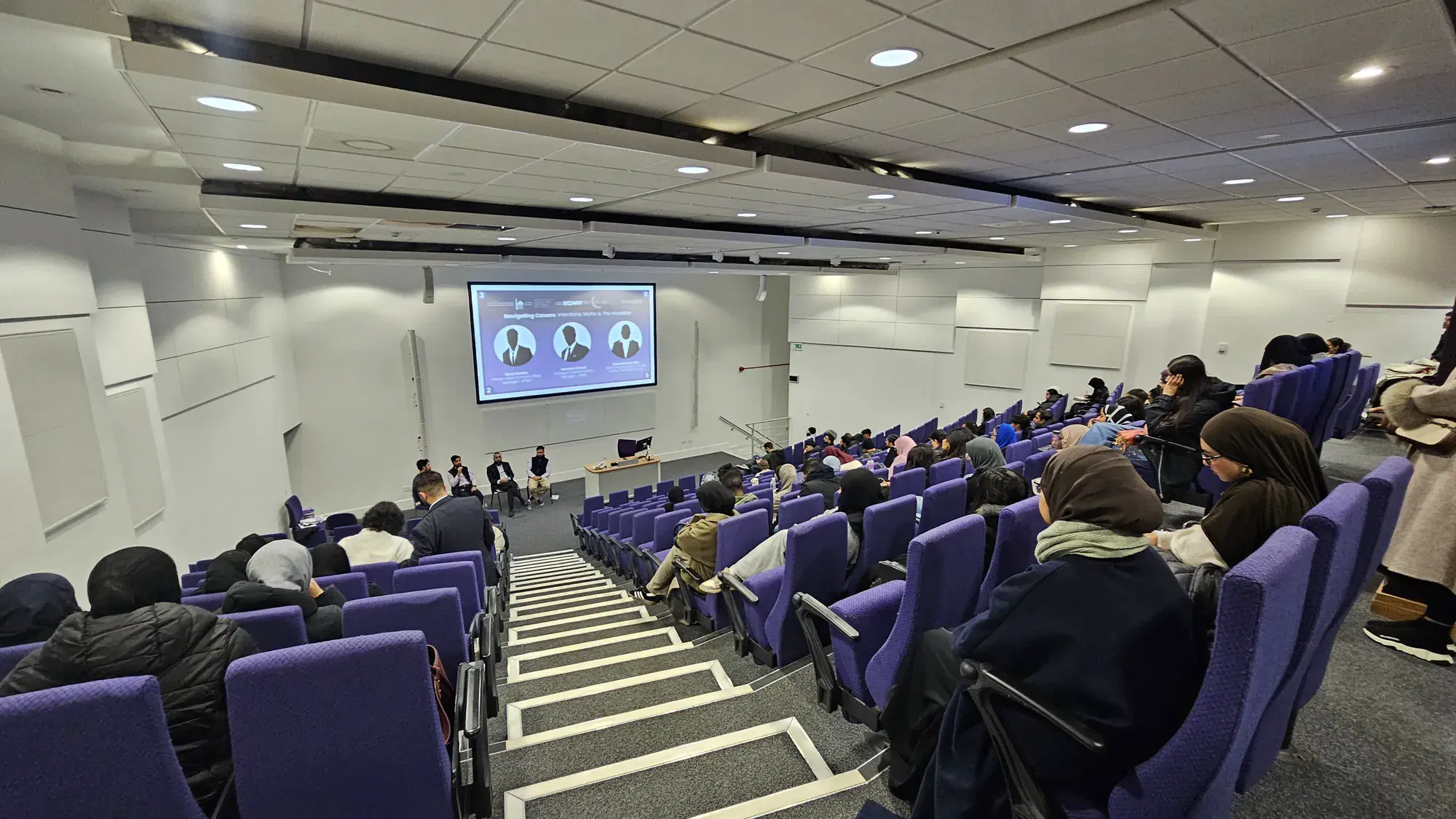 Students in a lecture theatre watching a panel at an IHSAAN career conference