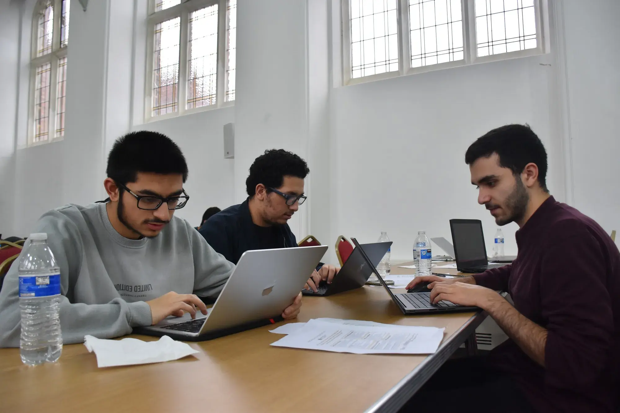 A team of three focused on laptops by the windows