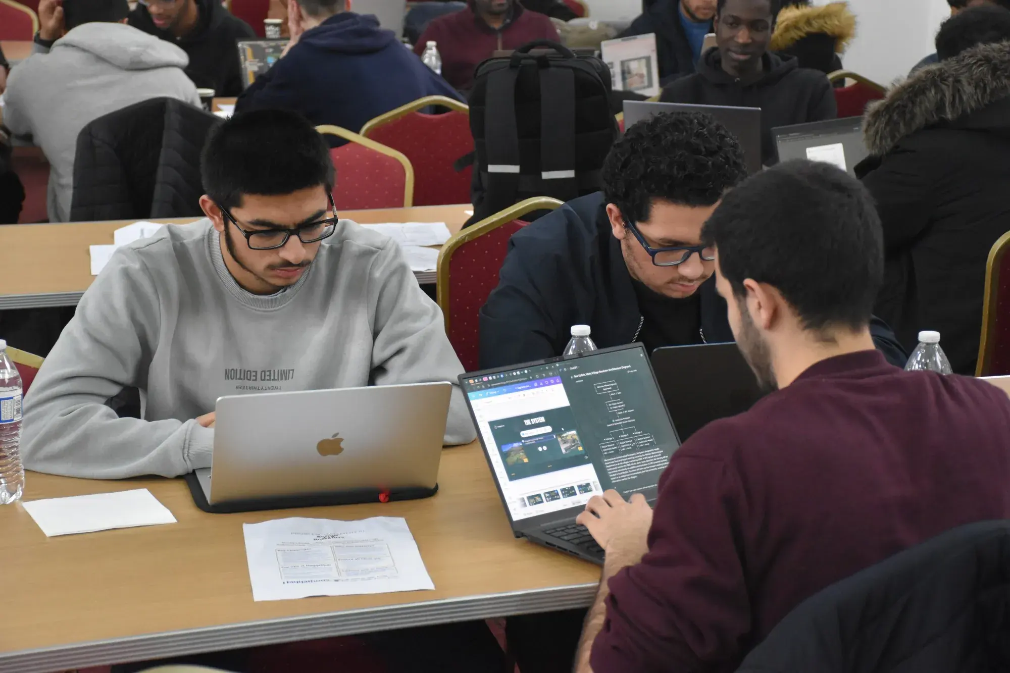 Three students coding together at a shared hackathon table